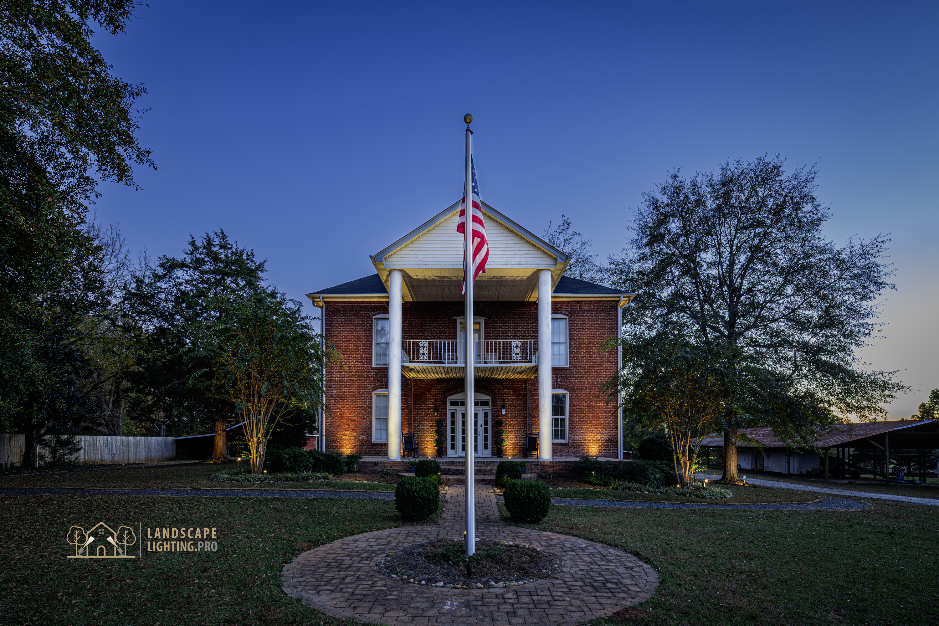 A wide view of the historic home and its lit grounds at dusk