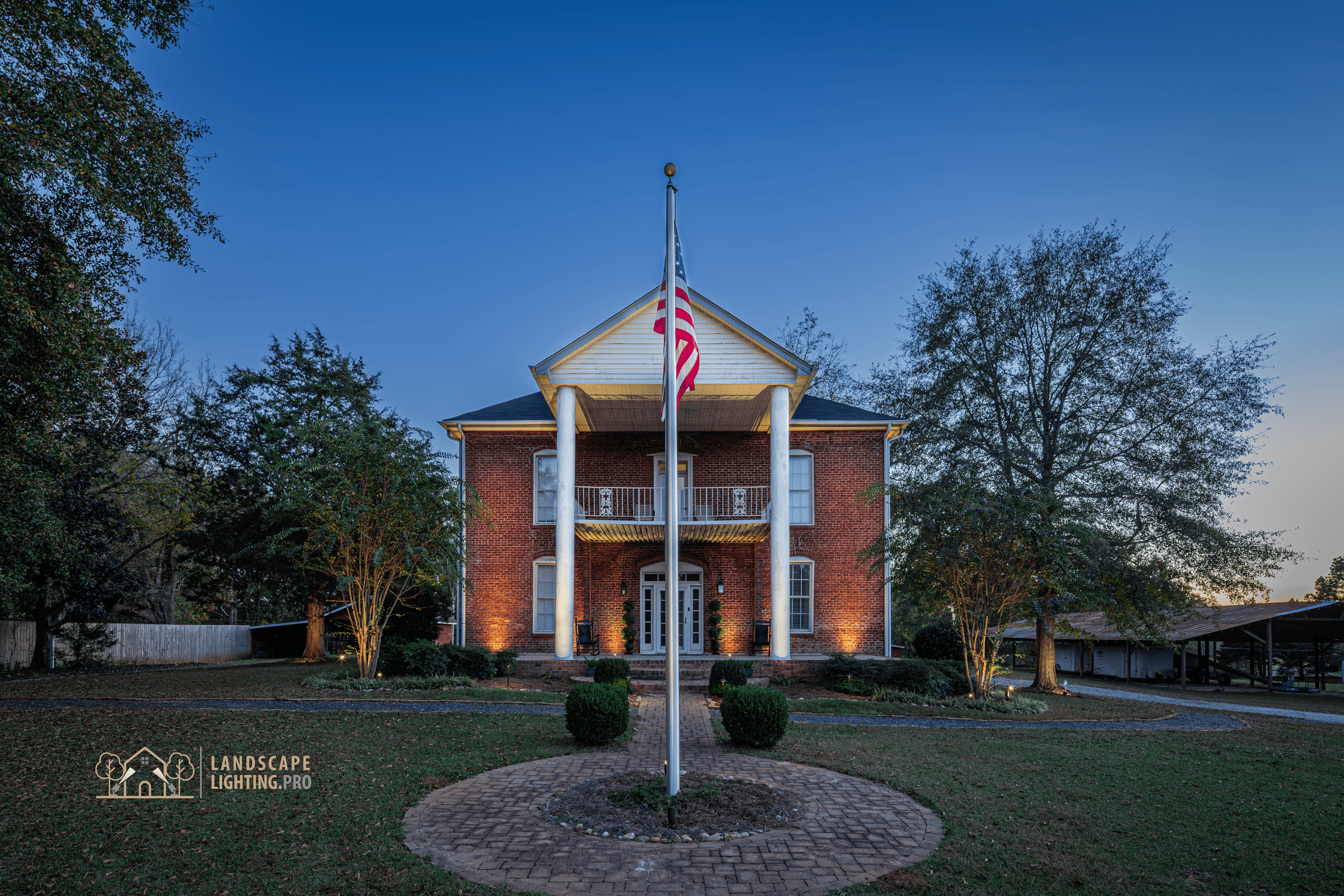 A wide view of the historic home and its lit grounds at dusk