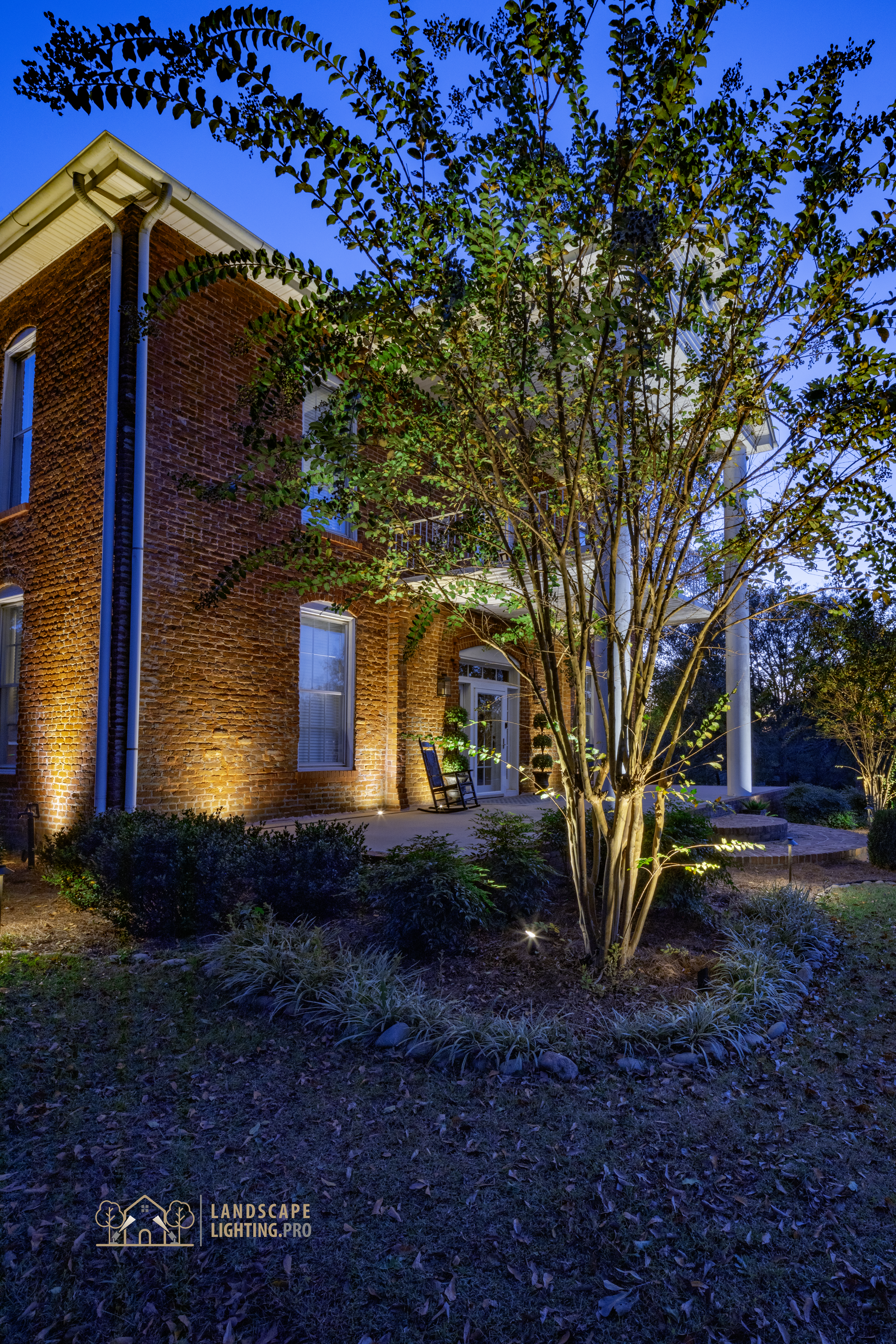 A vertical view of the historic home's lit landscape and trees at dusk