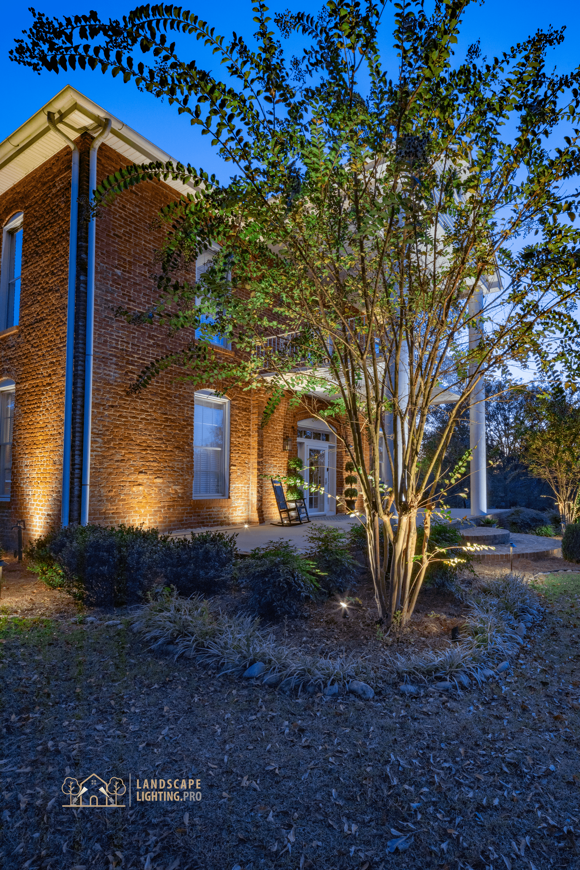 A vertical view of the historic home's lit landscape and trees at dusk