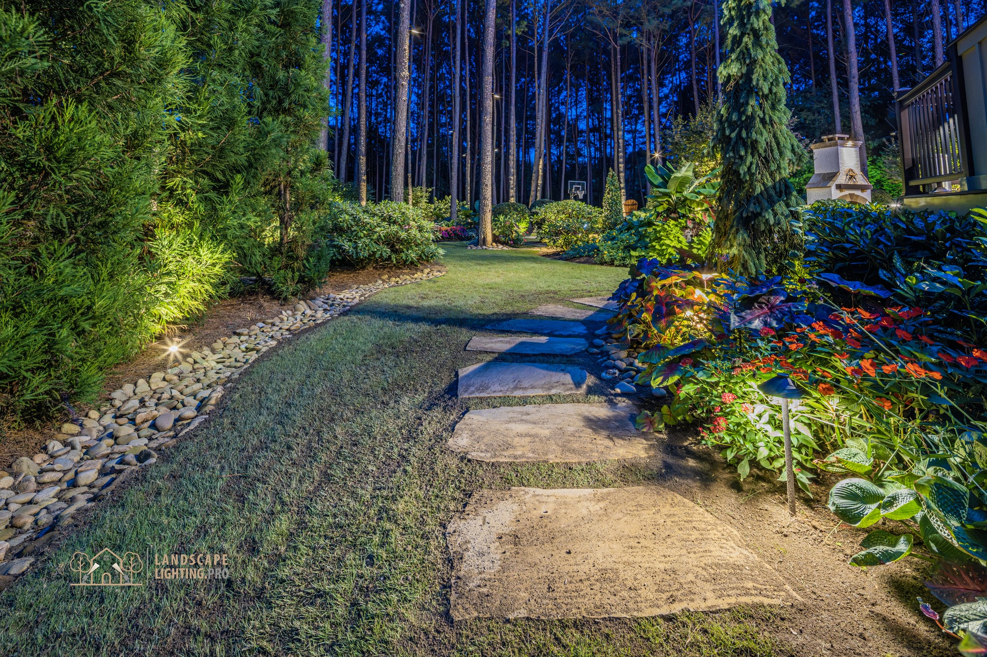 Flagstone stepping stones set into manicured lawn, with a river-rock dry-edge bed border at dusk