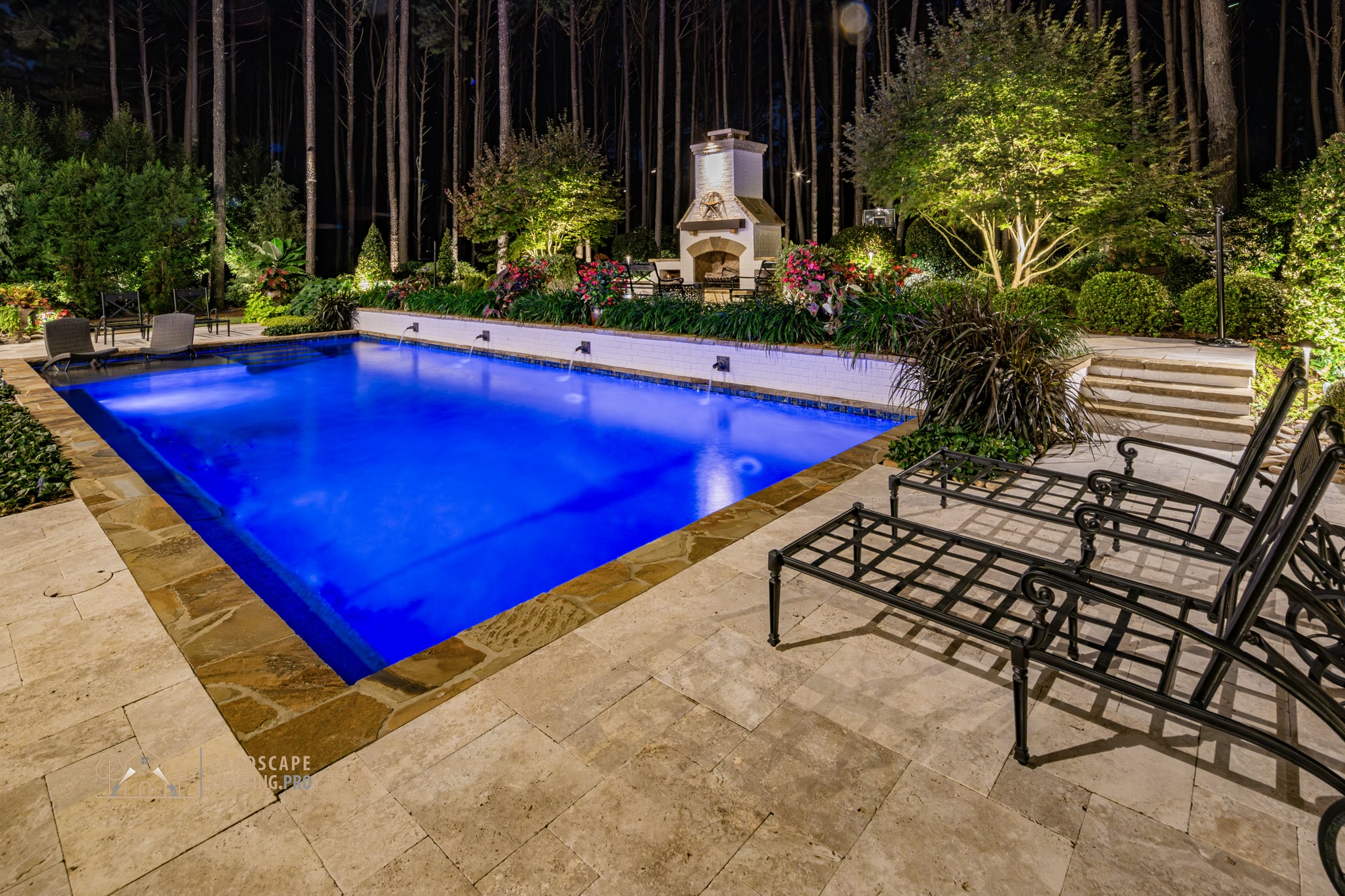 A view across the lit travertine patio toward the surrounding plantings at night