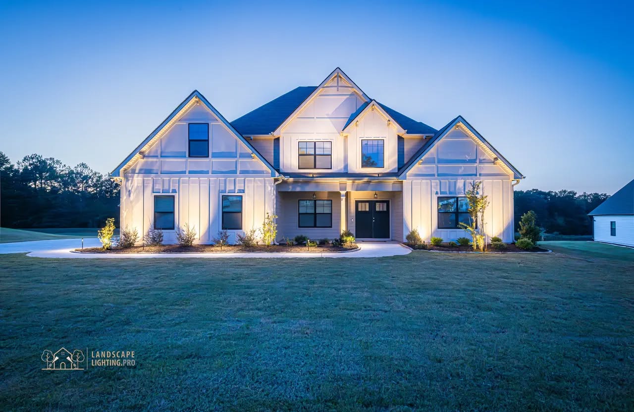 A modern farmhouse in Senoia illuminated at dusk with layered architectural uplighting across three gables